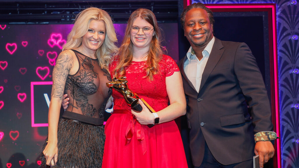 Lina Love mit Venus Award 2022 Trophäe zwischen Moderatorin RoxxyX und Moderator Mola Adebisi auf der Bühne
